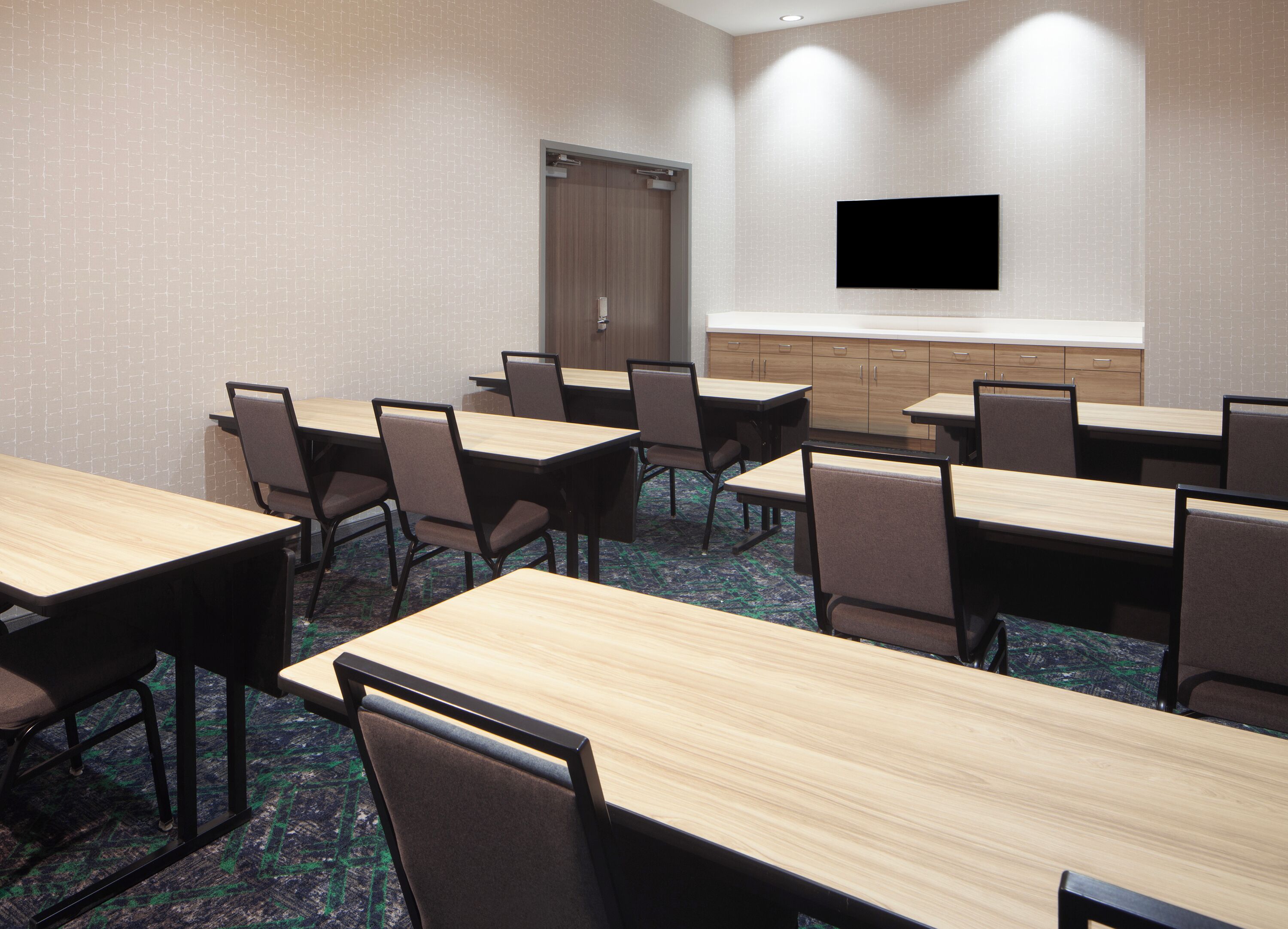 A conference room with multiple tables and chairs, a television on the wall, and a door in the background.