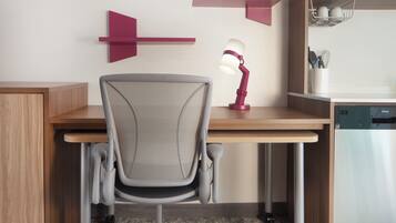 A modern office chair with a mesh backrest, a desk with a wooden finish, and a red desk lamp.