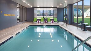 Une piscine intérieure à l’eau d’un bleu cristallin, entourée de chaises longues et d’une table placée au bord du bassin.