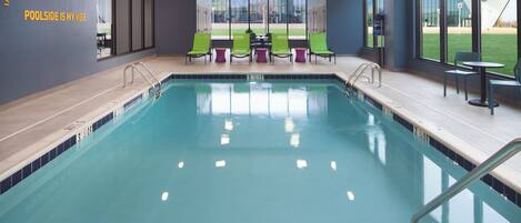 An indoor swimming pool with clear blue water, surrounded by lounge chairs and a poolside table.