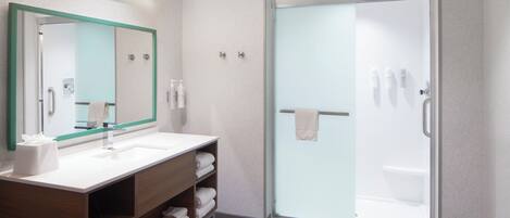 Un baño moderno con ducha de vidrio, tocador de madera con espejo y un perchero para toallas.