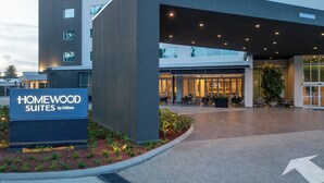 Entrada de hotel con el letrero de Homewood Suites by Hilton, un área de estar al aire libre techada y un camino despejado hacia la entrada.