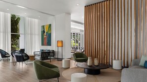 Un salón moderno con una mesa de centro redonda, sillones verdes y un sofá gris. Hay un ventanal con cortinas de gasa y vistas a zonas verdes.