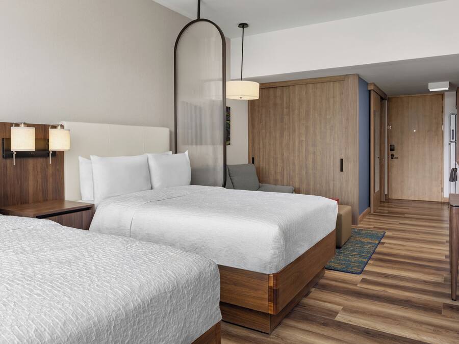 Hotellihuone, jossa on kaksi sänkyä, työpöytä, tuoli, vaatekaappi ja pieni keittiönurkkaus.