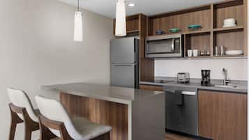 A modern kitchen with a central island, bar stools, a microwave, a refrigerator, and a coffee maker.