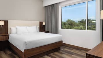 Habitación de hotel moderna con una cama grande, cabecera de madera y vistas a un paisaje urbano a través de un amplio ventanal.