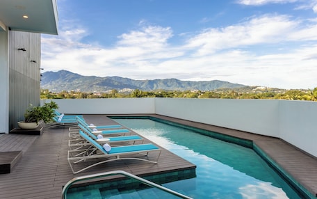 A rooftop pool with lounge chairs and a view of mountains.