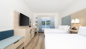 Habitación de hotel con cama, escritorio, silla, televisor y ventana con cortinas.
