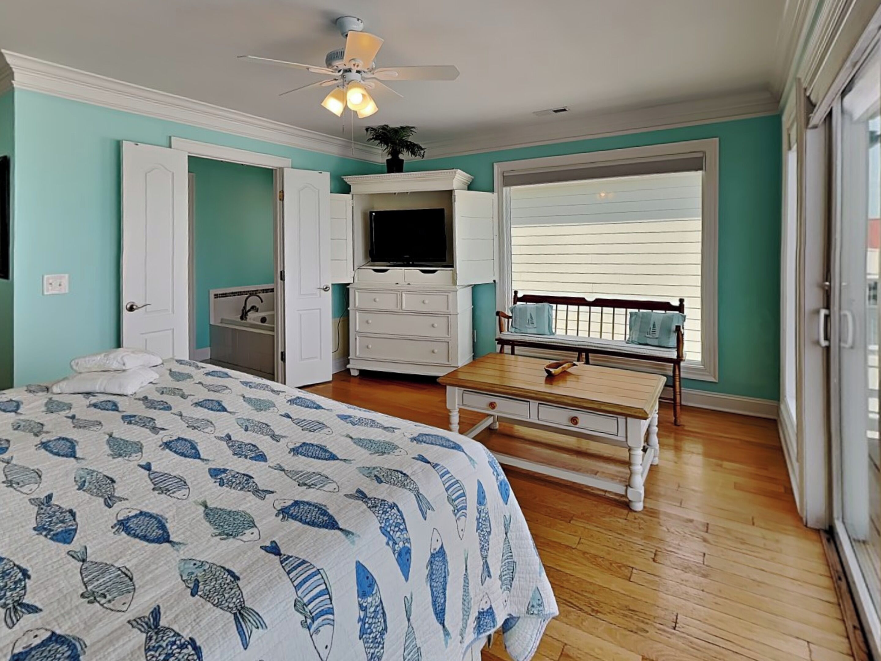 A bedroom with a bed, a dresser, a television, and a window with blinds.