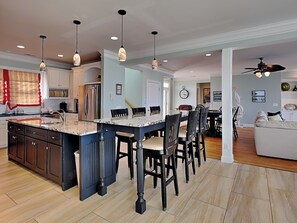 A spacious kitchen with a large island, dark wooden chairs, and pendant lighting. - Big Kahuna by Carolina Retreats (Kure Beach)
