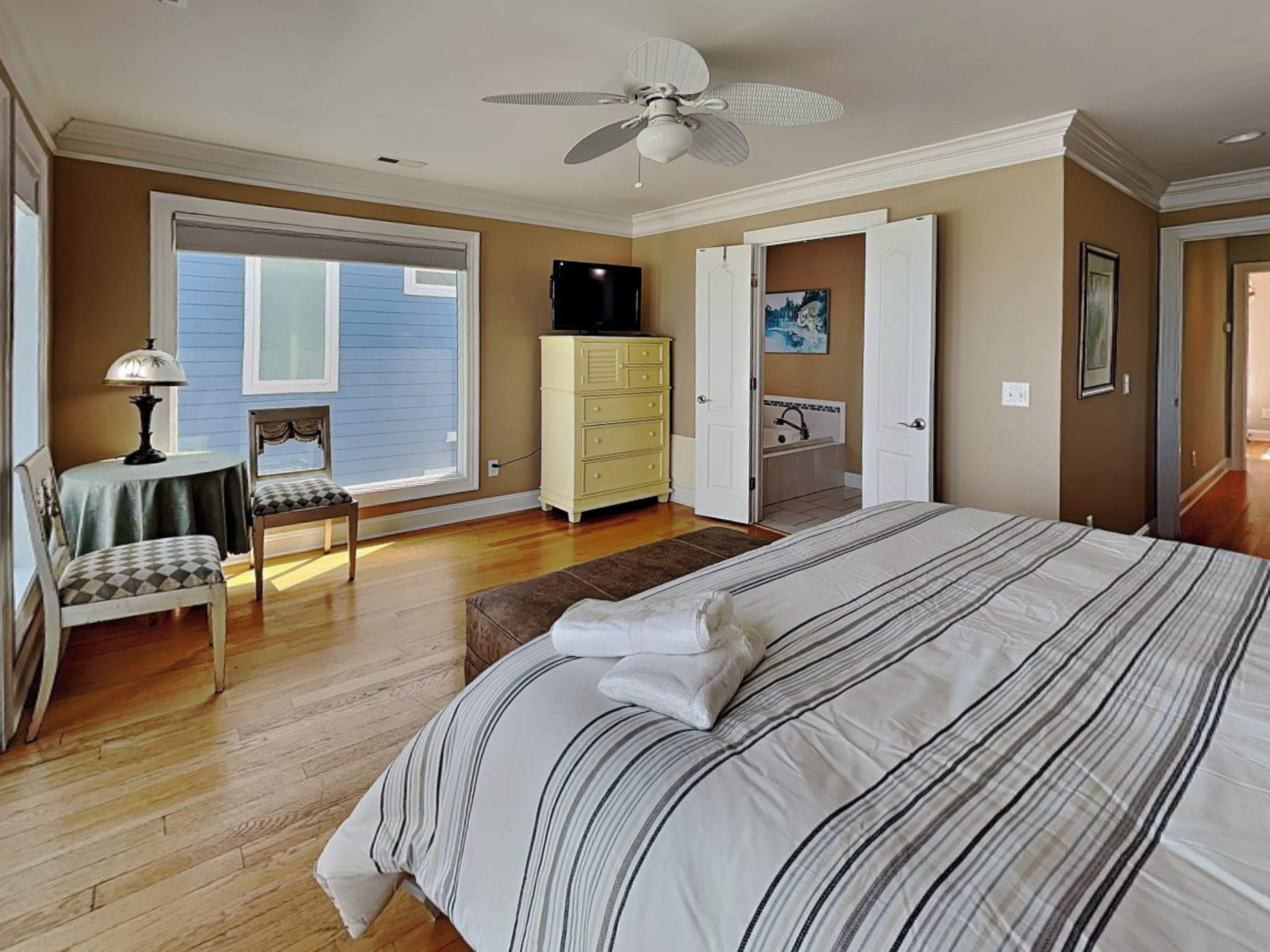 A bedroom with a large bed, a dresser, a chair, a desk, and a ceiling fan.