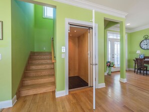 A staircase leading to an elevator in a room with green walls and wooden floors. - Big Kahuna by Carolina Retreats (Kure Beach)