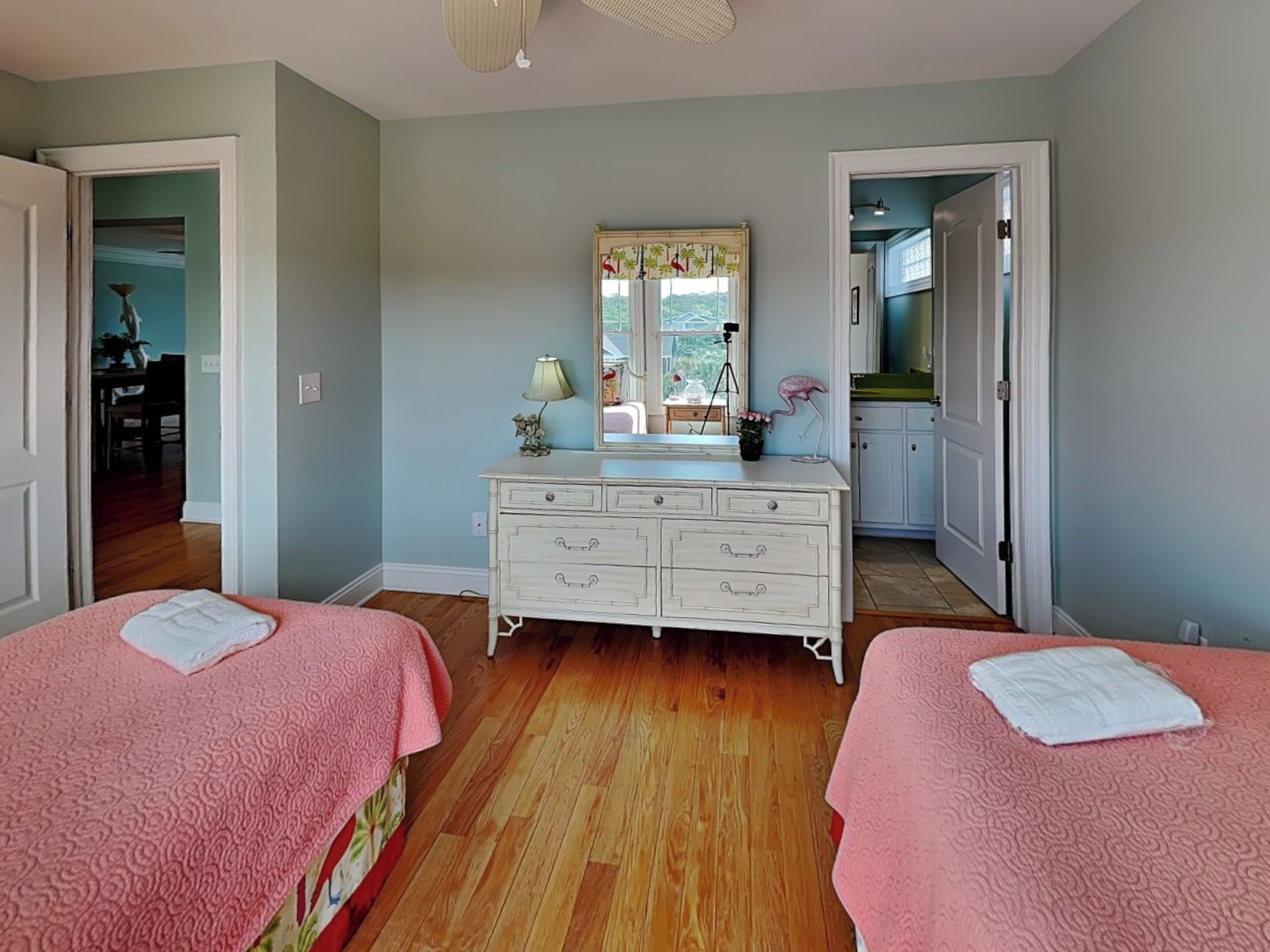 A bedroom with two beds, a dresser, a mirror, and a window.