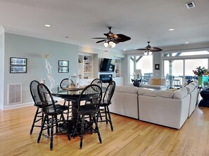 A spacious living area with a dining table, black chairs, a white sofa, and a ceiling fan. - Big Kahuna by Carolina Retreats (Kure Beach)