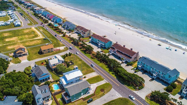Vista aérea de una zona residencial costera con casas, una playa y una carretera.