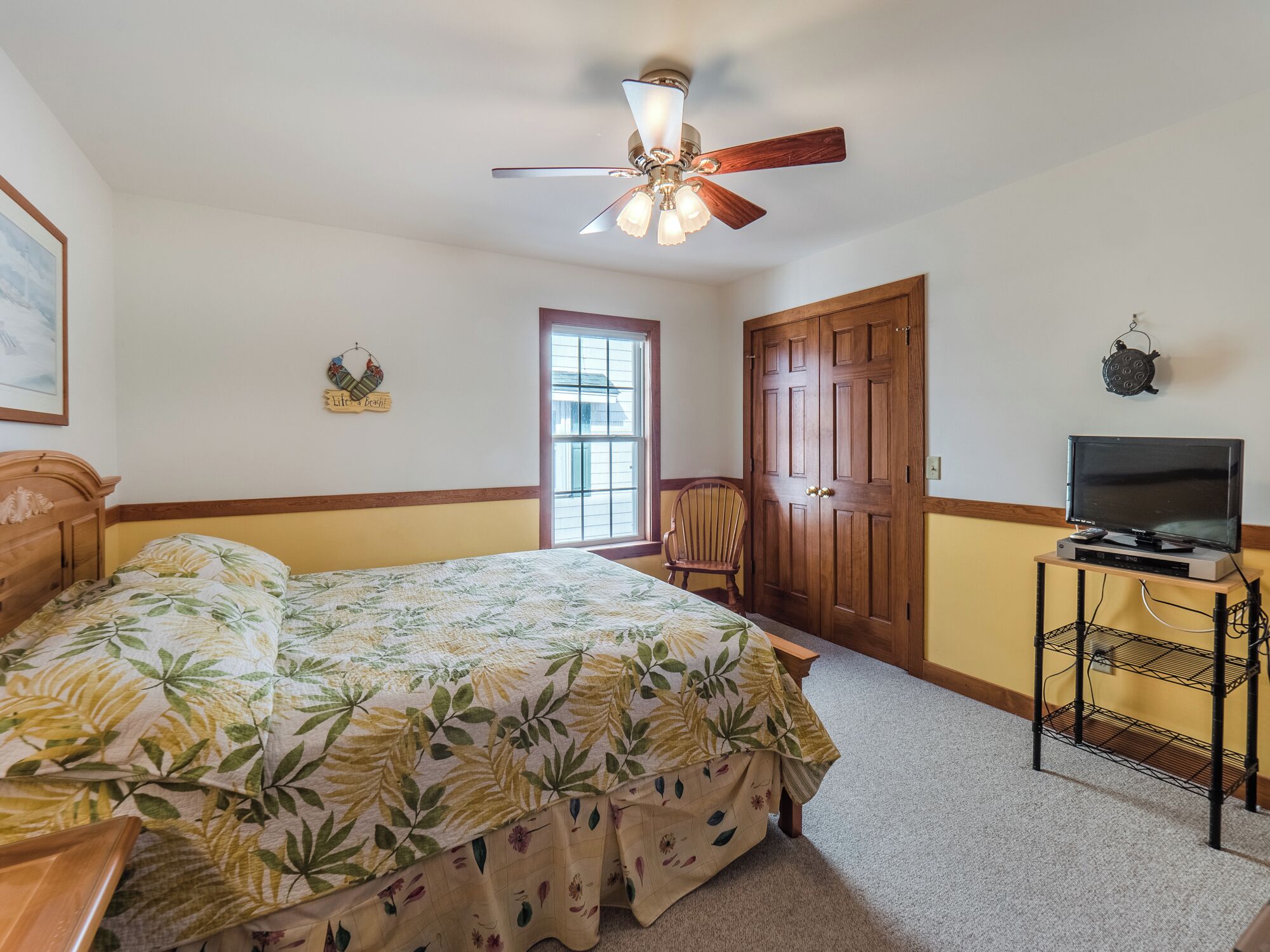 A bedroom with a bed, a ceiling fan, a television on a stand, and a door.
