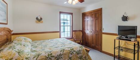 A bedroom with a bed, a ceiling fan, a television on a stand, and a door.