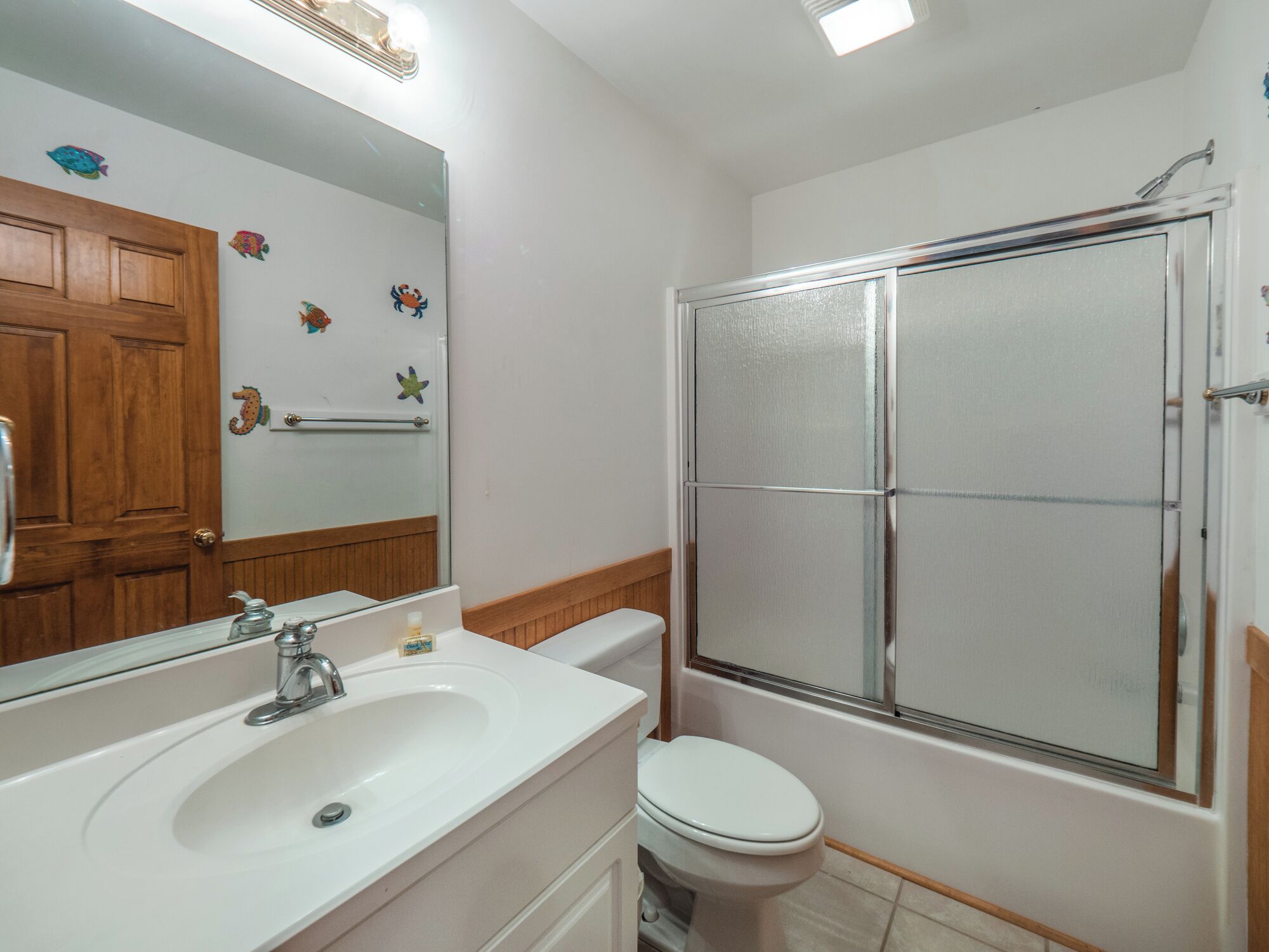 A bathroom with a white sink, a toilet, a glass shower enclosure, and a wooden door.