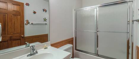 A bathroom with a white sink, a toilet, a glass shower enclosure, and a wooden door.