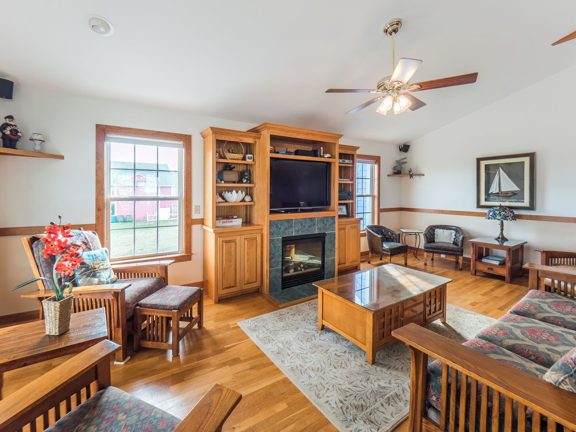 A spacious living room with wooden furniture, a fireplace, a television, and a ceiling fan.