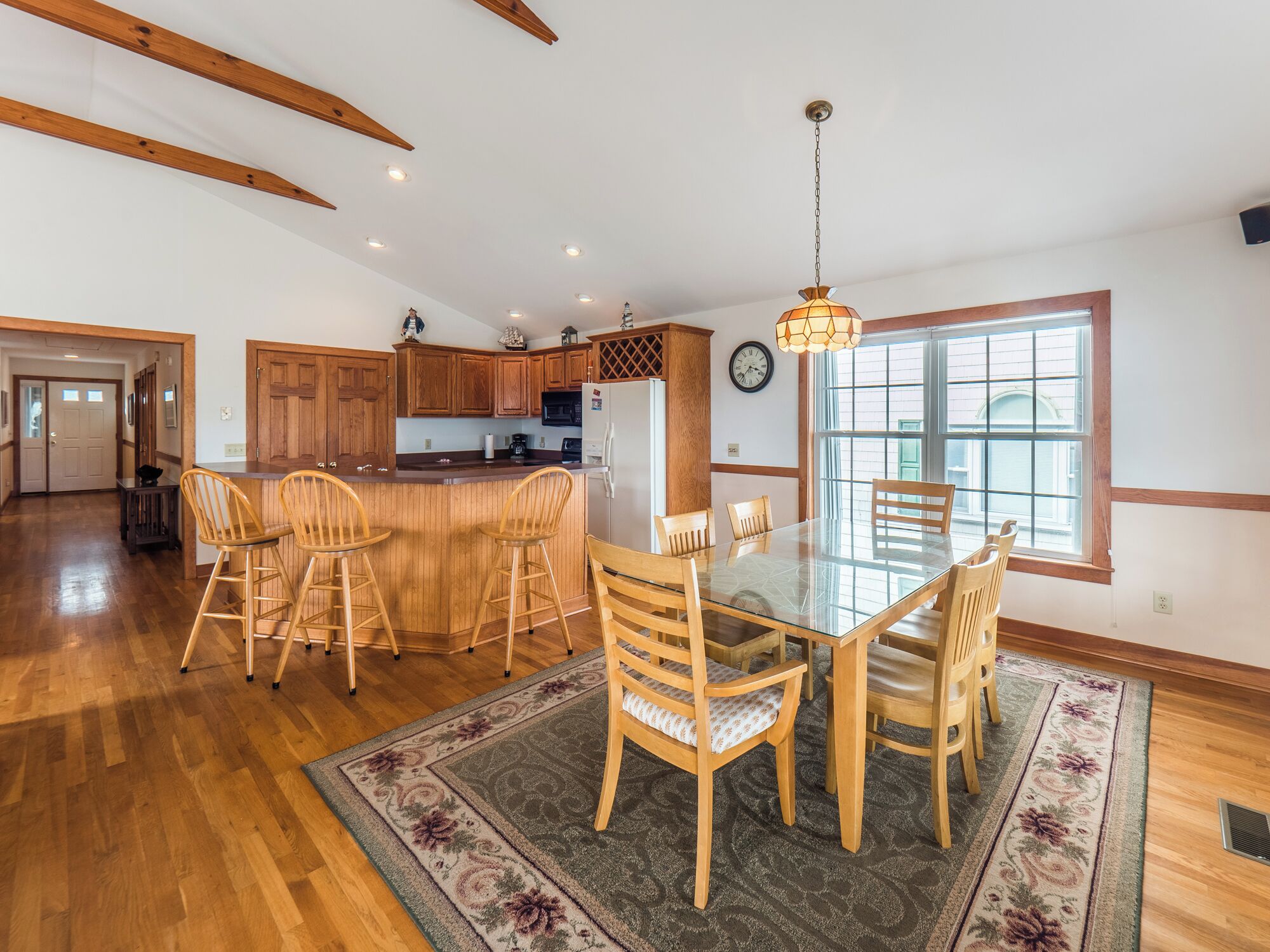 A spacious kitchen with wooden cabinets, a central island with stools, and a large dining table.