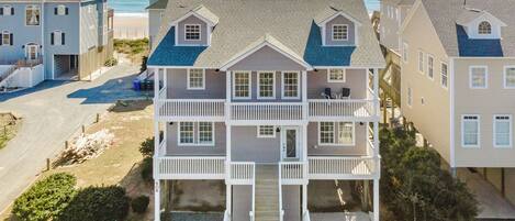 A multi-story beachfront property with balconies, a covered front porch, and a driveway leading to the entrance.
