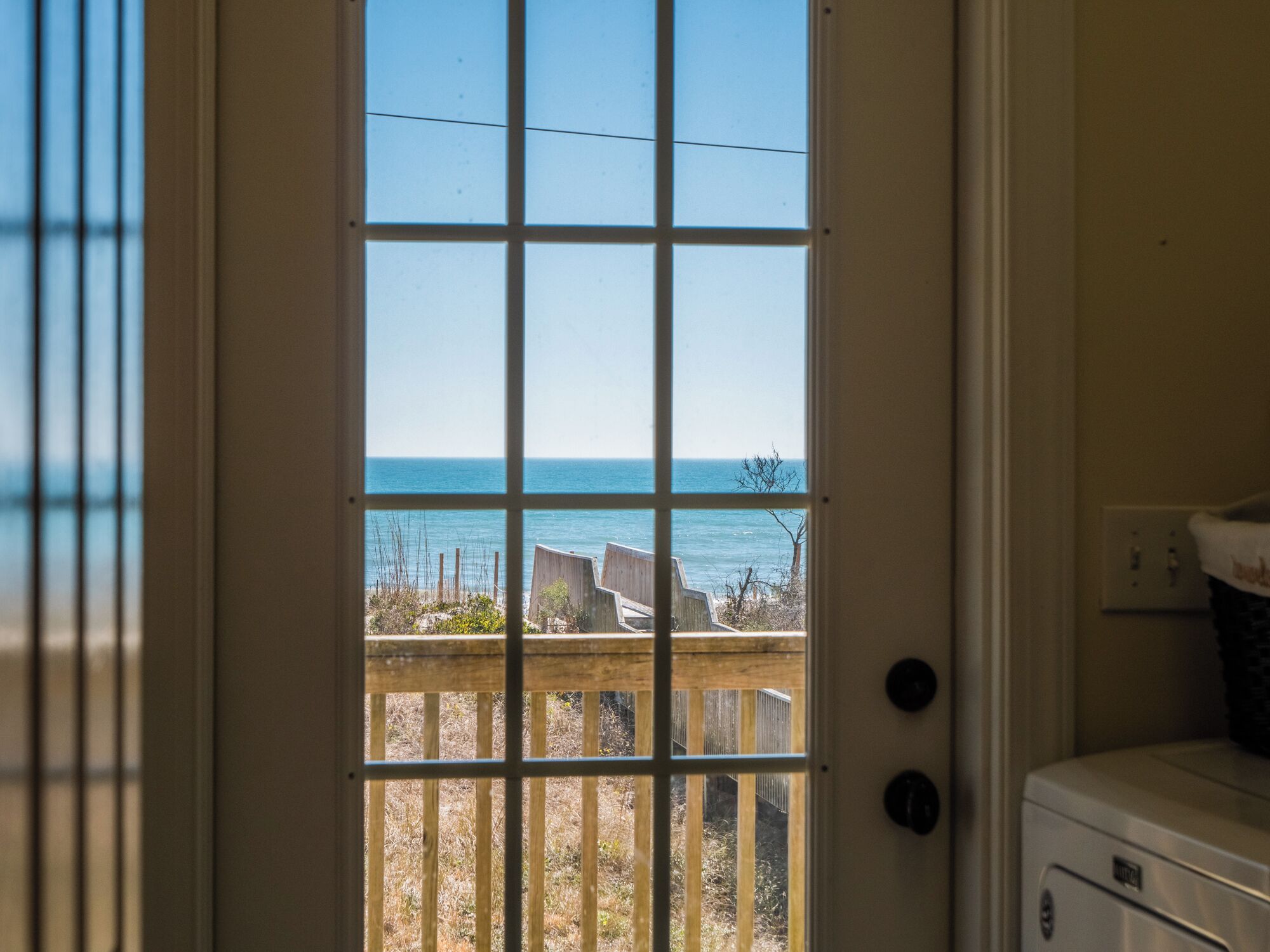 Blick durch ein Fenster auf ein Holzdeck und einen klaren, blauen Himmel.