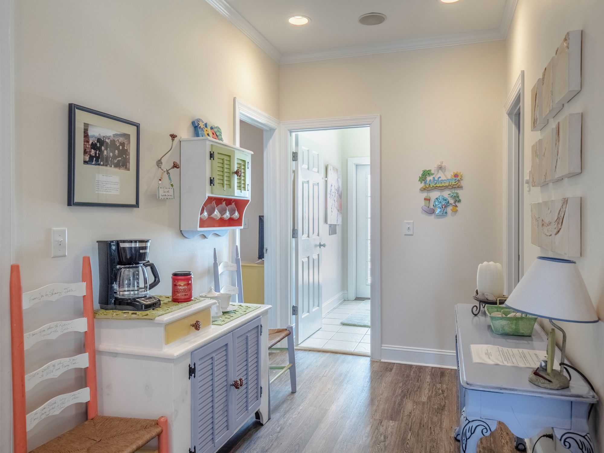 A hallway with a coffee machine, a cabinet with a green door, a framed picture on the wall, and a welcome sign.