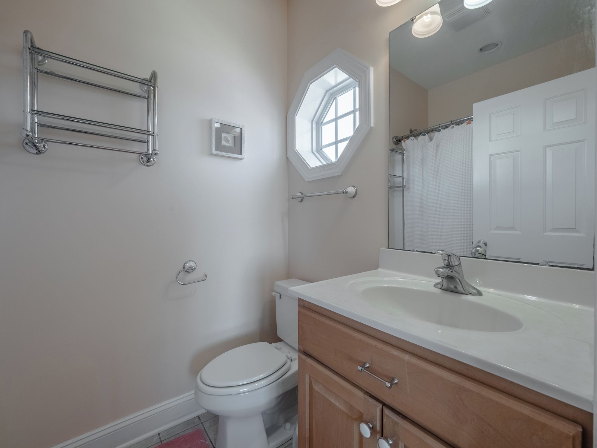 A bathroom with a white toilet, a wooden vanity with a sink, a mirror, and a towel rack.