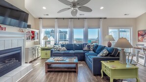 Ein geräumiges Wohnzimmer mit einem großen blauen Sofa, einem Kamin, einem Deckenventilator und Meerblick.