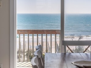 Udsigt fra en balkon over havet, med et træbord og stole i forgrunden.