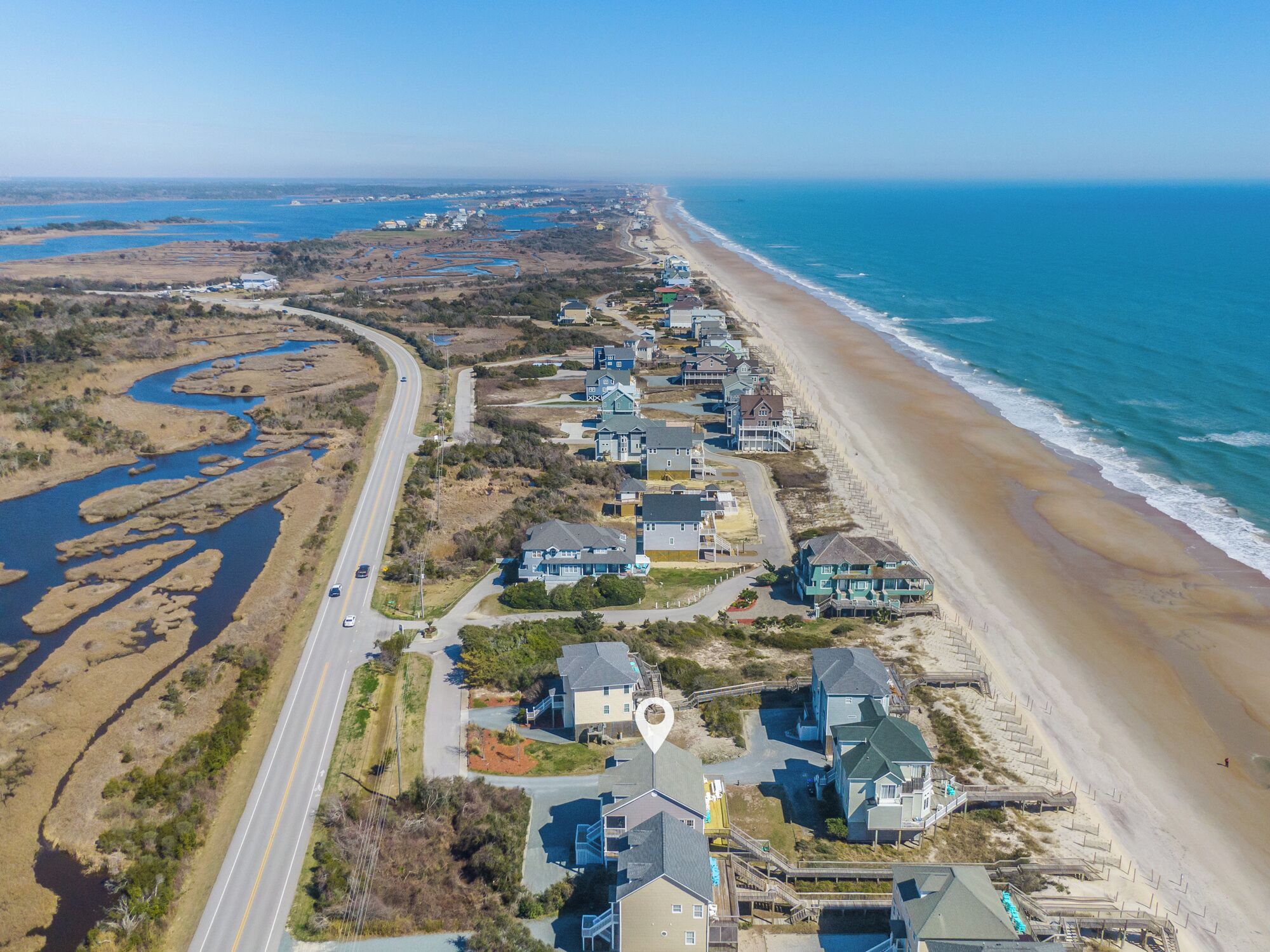 An aerial view of a coastal residential area with houses along the beach, a road, and a water body.