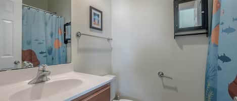 A bathroom with a white sink, a mirror, a framed picture on the wall, and a shower curtain with a fish pattern.
