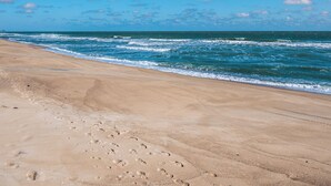 A beach with footprints leading to the water, a clear sky, and waves crashing onto the shore. - Shoo Fly by Carolina Retreats (Kure Beach)