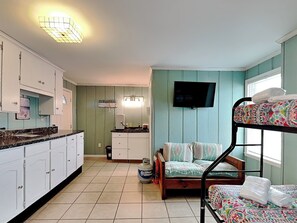 A compact room with a bunk bed, a kitchenette, and a television. - Shoo Fly by Carolina Retreats (Kure Beach)