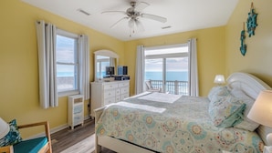 A bedroom with a bed, a desk, a chair, a ceiling fan, and a view of the ocean. - Sunflower Beach House by Topsail Realty (Holly Ridge)