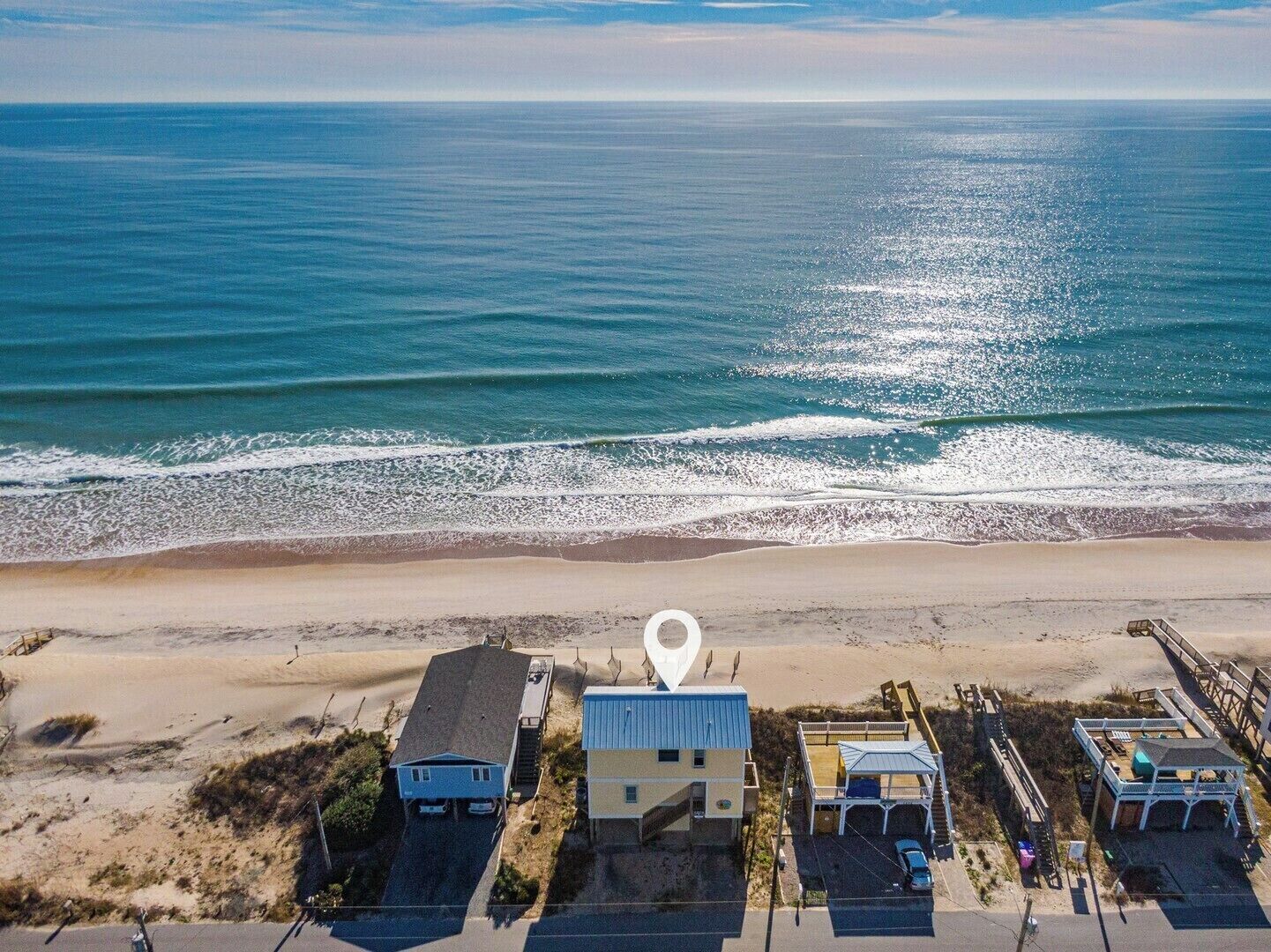 Luchtbeeld van een pand aan het strand, met een groot wit bord dat een locatie aangeeft.