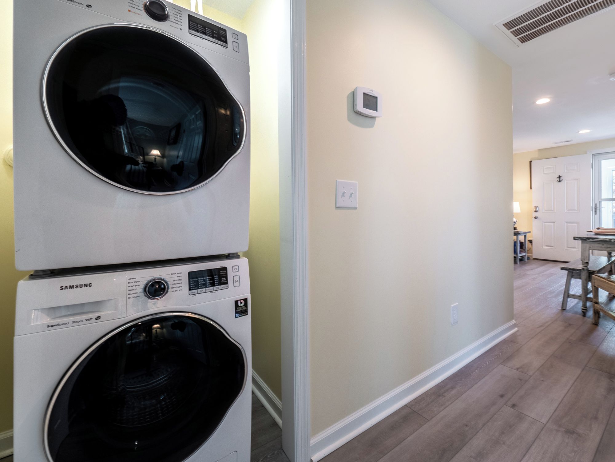A laundry room with two stacked front-loading washing machines and a wall-mounted thermostat.