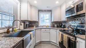 A modern kitchen with white cabinets, granite countertops, stainless steel appliances, and a window with blinds. - Ankers Away by Topsail Realty (Holly Ridge)