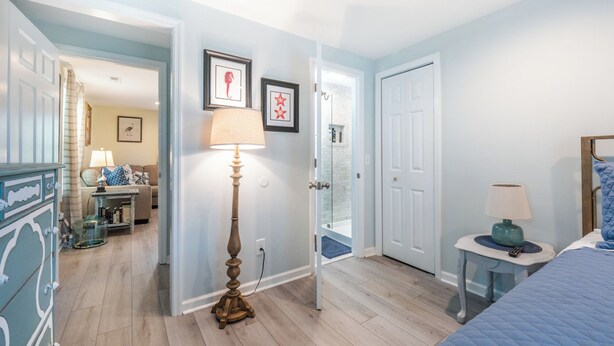 A bedroom with a bed, bedside tables, a lamp, and a door leading to a bathroom. - Ankers Away by Topsail Realty (Holly Ridge)