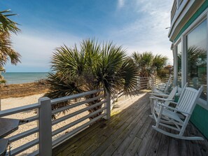 Eine Holzterrasse mit weißen Schaukelstühlen mit Blick auf einen Strand.