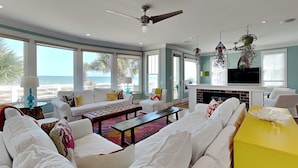 A spacious living room with a large sofa set, a coffee table, and a yellow accent table. There is a fireplace and a television. - A Shore Cure by Carolina Retreats (Kure Beach)