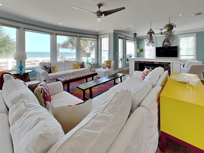 A spacious living room with a large sofa set, a coffee table, and a yellow accent table. There is a fireplace and a television.