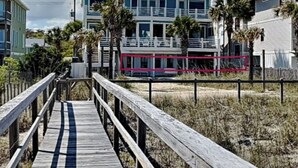 A beachfront property with a wooden boardwalk leading to a multi-story building with balconies and a pool area. - A Shore Cure by Carolina Retreats (Kure Beach)