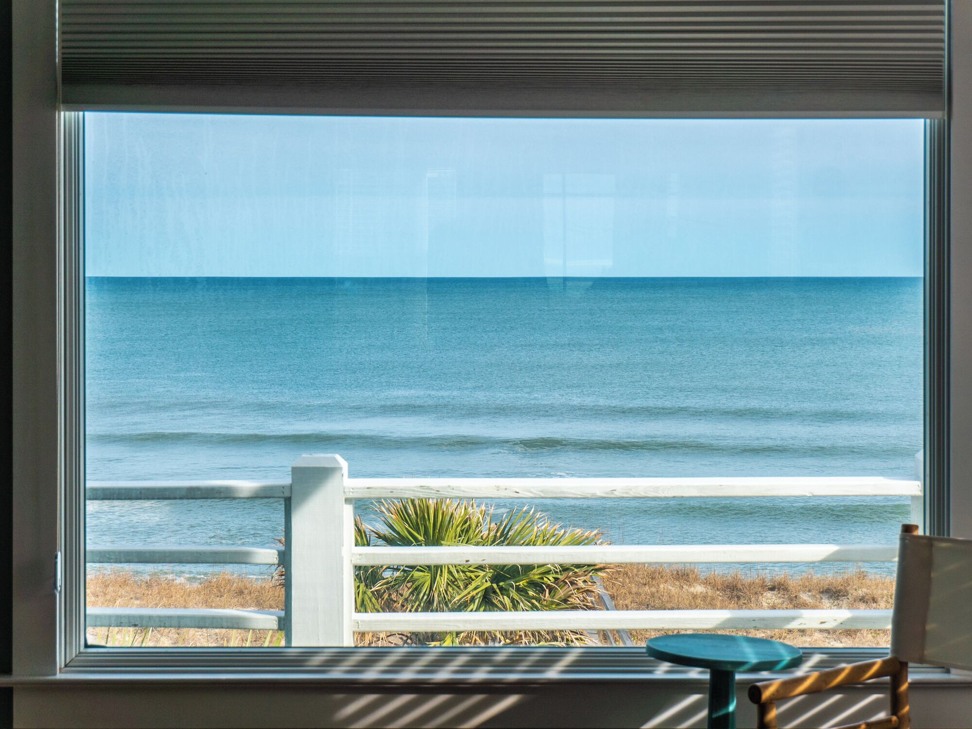 A view of the ocean through a window with a white railing and a chair.