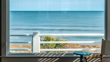 A view of the ocean through a window with a white railing and a chair.