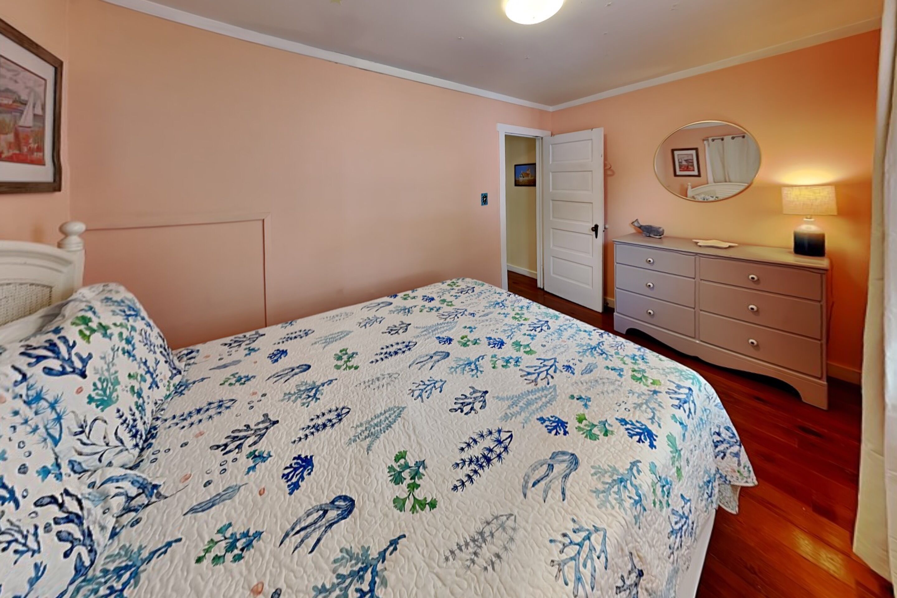 A bedroom with a bed, dresser, mirror, and door.