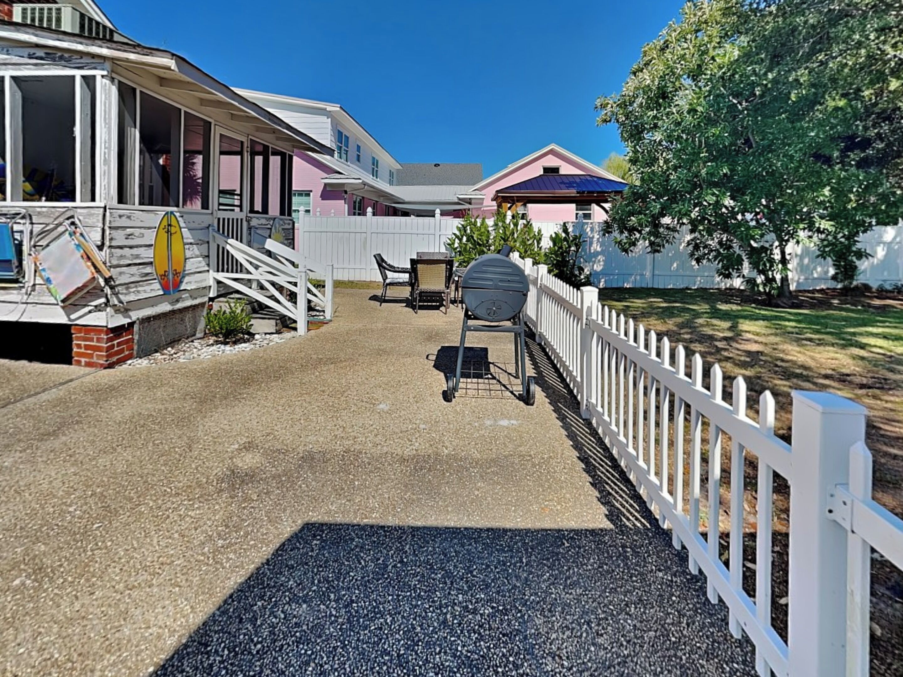 A residential area with a covered porch, a barbecue grill, and a white picket fence.