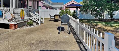 A residential area with a covered porch, a barbecue grill, and a white picket fence.