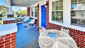 A covered porch with a blue door, white outdoor furniture, and a patterned rug. - CB Sunshine Cottage by Carolina Retreats (Carolina Beach)